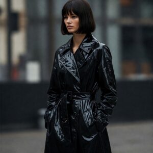 A long black rain coat with a belted waist, highlighting its elegant and figure-flattering silhouette.
