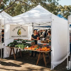 A scene depicting a white 4x4 pop up canopy being used as a vendor booth at a farmer's market, with side walls for added privacy and branding.