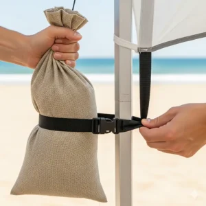 An image showing the process of attaching a filled sand bag to the corner of a beach tent pole with a sturdy strap.