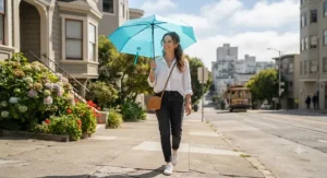 A woman holding a lightweight travel umbrella while walking down a sunlit sidewalk in San Francisco.
