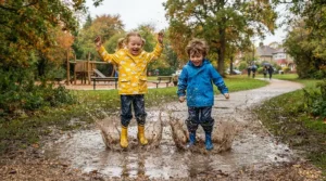 Happy children splashing in park puddles while wearing a colorful family rain gear set in the autumn.
