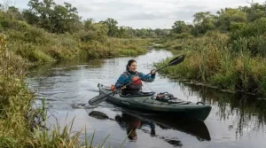 A kayaker paddling through marshlands wearing lightweight fishing gloves waterproof for grip.