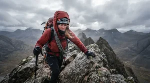 Climber enduring high winds on a rocky peak with the hood of their 800 fill down jacket for backpacking securely fitted.